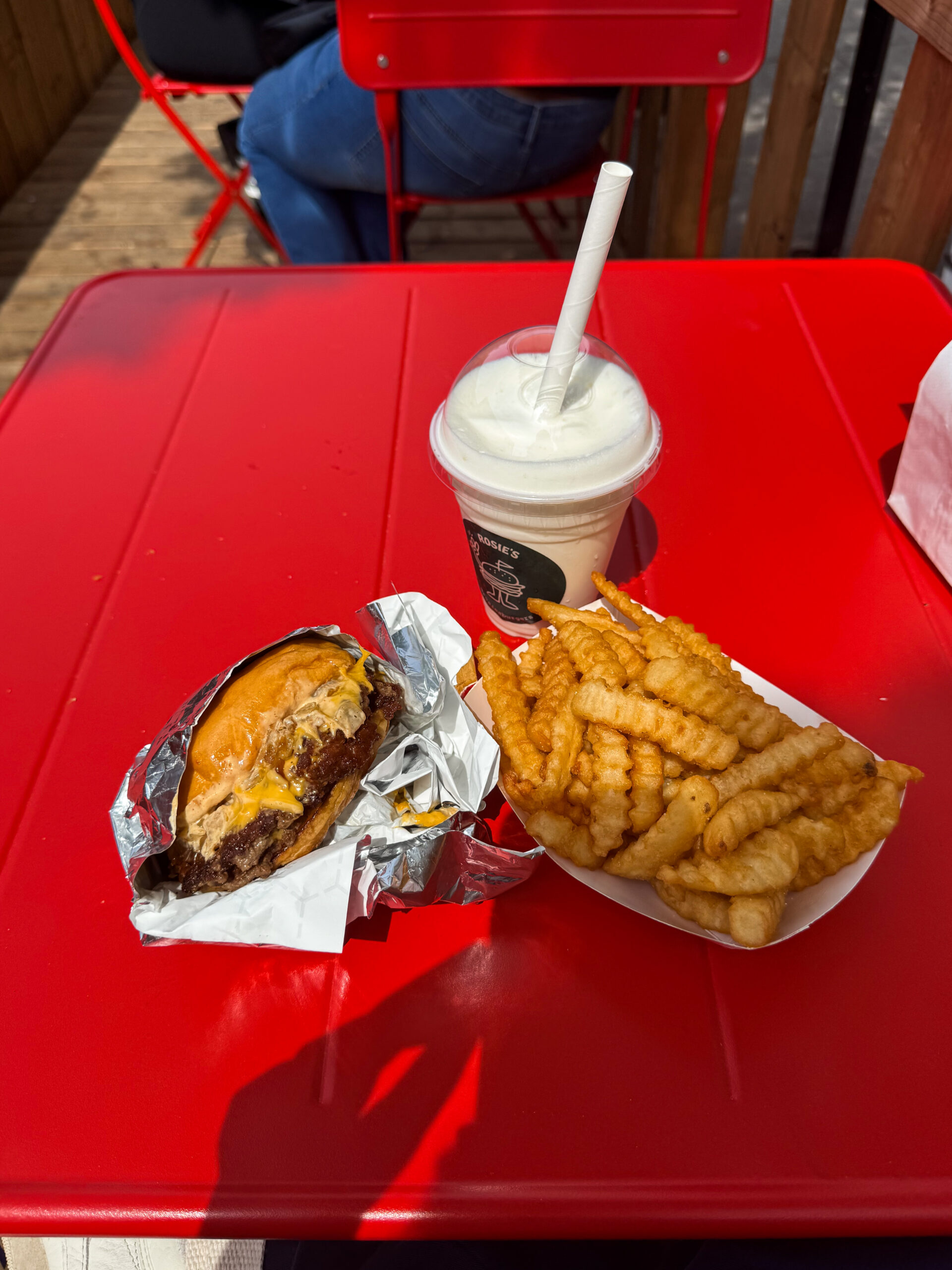 burger, fries, and milkshake on red outdoor table.
